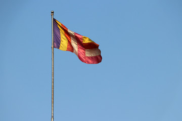 Fabric Buddhist flag blown by wind on the flagpole with blue sky background.