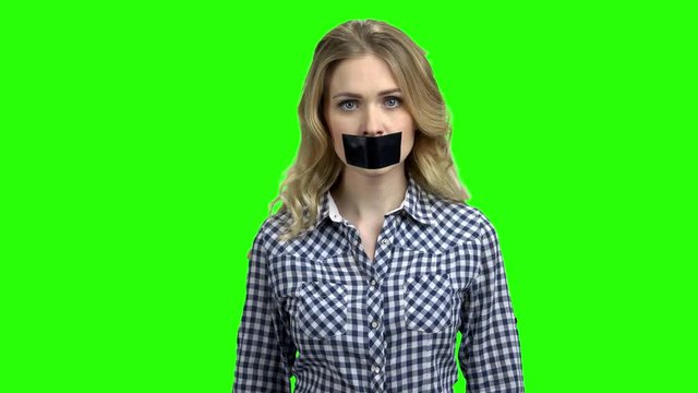 Young angry woman with black tape on her mouth. Young emotional woman with tape across mouth on green screen background. Freedom of speech concept.