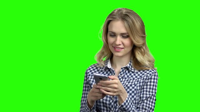 Woman using phone on green screen background. Happy girl in checkered shirt using smartphone with smile. Technology, internet, communication and people concept.