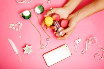 woman hands holding macaroons with lot of girl stuff on pink background, girls accessories concept close up