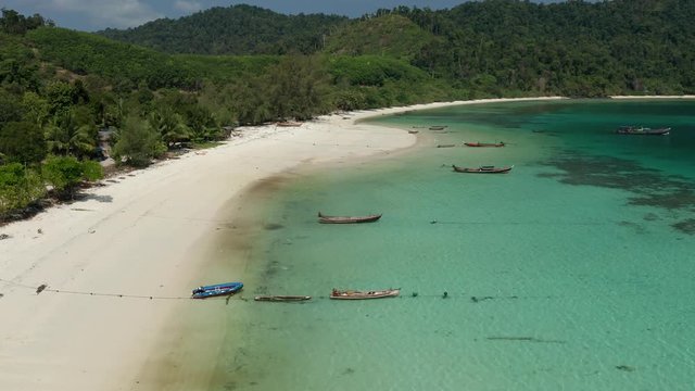 Aerial drone view flying along a tropical island with sandy beach and traditional wooden boats (Swinton Island, Myanmar)