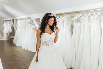 Beautiful young brunette woman choosing wedding dress in a bridal salon.