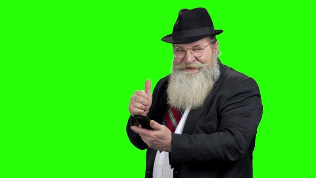 Senior man looking at phone and showing thumb up. Old happy man holding mobile phone and giving thumb up. Green Chroma Key background.