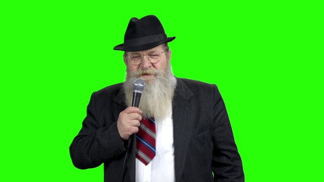 Elderly businessman talking on green screen. Confident senior man in classic suit talking into microphone and looking at camera. Alpha Channel background.