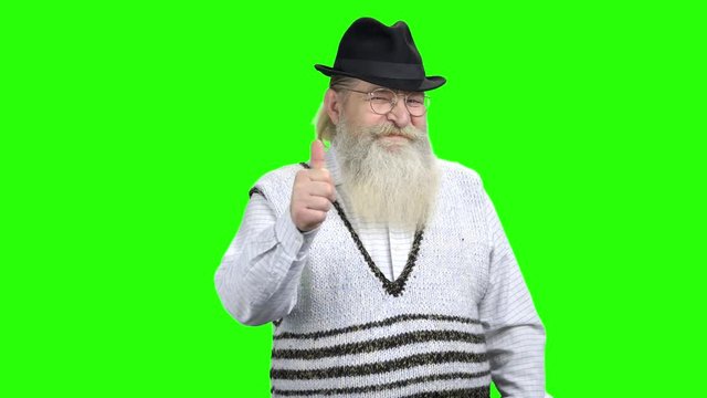 Smiling senior man with beard showing thumb up. Happy elderly man in eyeglasses on green screen background. People and gestures concept.