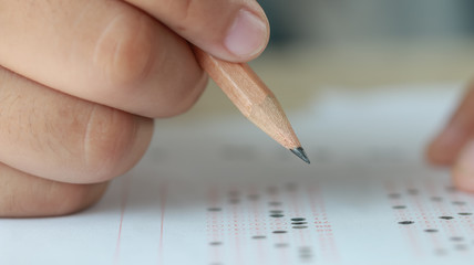 Education test in university or high school concept : Hands student holding pencil for testing exams on answer sheet, taking fill in exam document paper at campus classroom. Knowledge learning concept