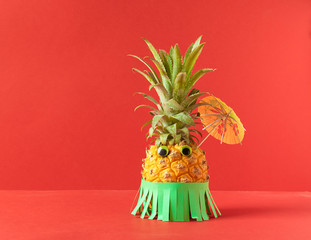 Ripe pineapple with eyes and a Hawaiian green skirt and umbrella on a trendy coral background. Summer holiday concept.