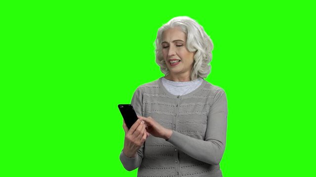 Smiling senior woman with smartphone on green screen. Attractive elderly woman surfing internet on mobile phone.