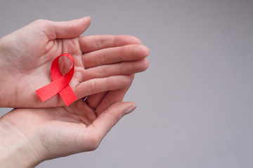 Girl’s hands holding red ribbon, symbol of  skin cancer, cancer awareness month.