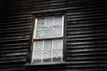A lace curtain in a window in an old unpainted clapboard house