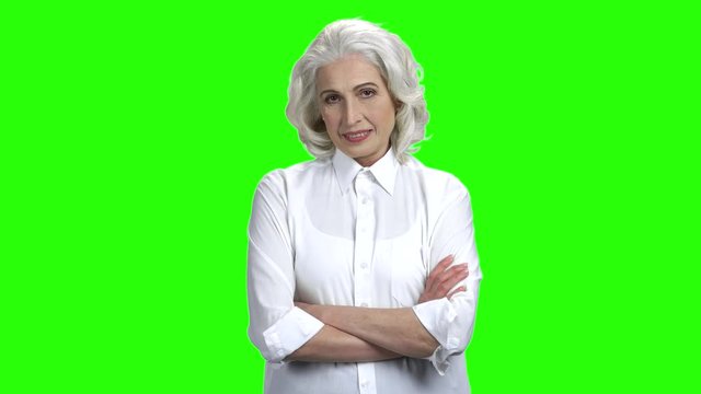 Smiling senior woman on green screen background. Gray haired elderly woman in elegant blouse crossed arms on chroma key background.