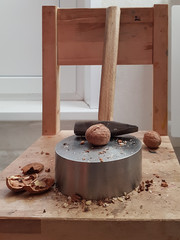 On a wooden chair there is a metal disc with a hole and a hammer for splitting walnuts.