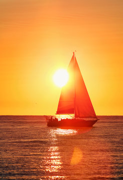Sailing yacht at sunset, sun setting behind the sail