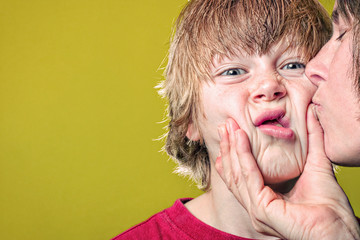Boy grimacing when his mother grabs his face while kissing him