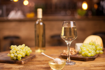 Close up of glass with white wine with sprigs of grapes on wooden table