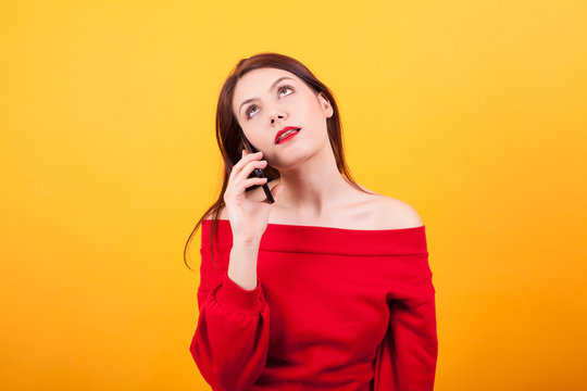 Portrait of beautiful young woman bored while talking on the phone over yellow background