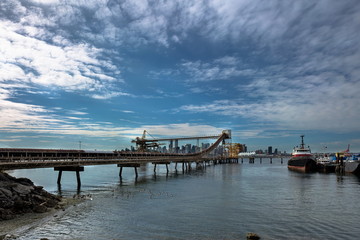 Fototapeta na wymiar Loading conveyor at the cargo terminal of the port in North Vancouver, the blue sea and a beautiful cloudy sky against the background of Vancouver downtown