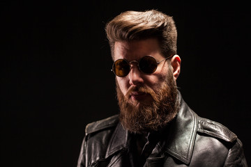 Elegant bearded man with leather jacket and sunglasses over black background