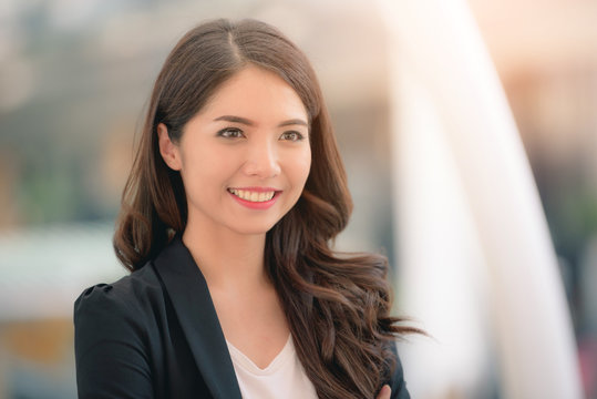 Portrait of a smiling asian businesswoman standing with arms folded on blurred city background. Business concept