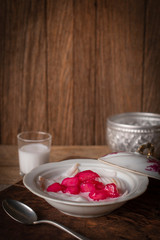 Thapthim krop, mock pomegranate seeds in coconut and syrup in the white bowl on the wood table there are spoon, coconut milk and water bowl placed around.