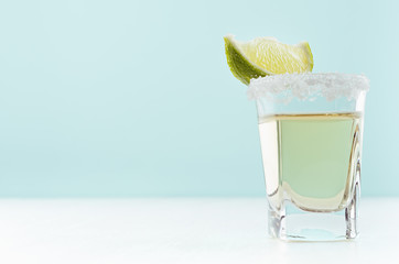Vacation summer shot drink - gold tequila in glass with lime and salt rim on white wood board and...