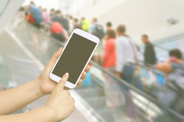 Hand hold and touch screen with people are going up the escalator in the Airport. Blur background.
