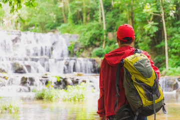 Young asian Tourist backpacker standing near a beautiful waterfall in forest and looking away. Image of camping,travel,hiker or recreation concept.
