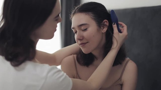 Lesbian woman combing hair her girlfriend. Happy lesbian couple sitting in the bed at home. Romantic relationship concept. Slow motion.