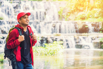 Young asian Tourist backpacker standing near a beautiful waterfall in forest and looking away. Image of camping,travel,hiker or recreation concept.