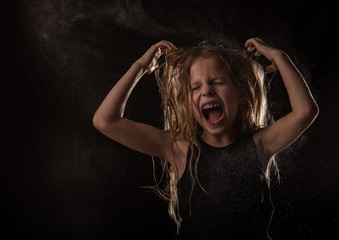 young girl with live emotions dancing under water drops. child screaming on a dark background with water splash