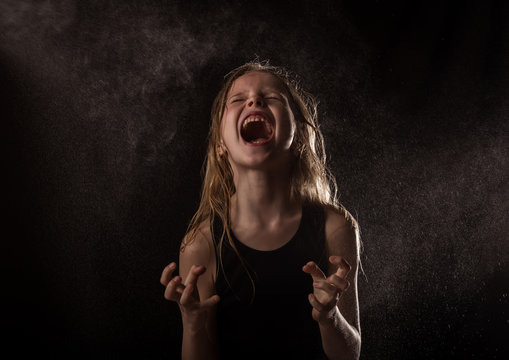 young girl with live emotions dancing under water drops. child screaming on a dark background with water splash