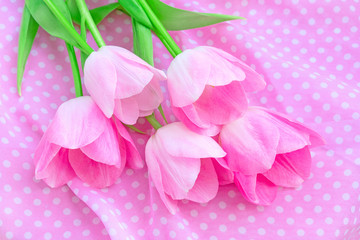 Arrangement of spring flowers with pink buds, lying on a pink fabric with white polka dots. View from above