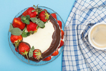 Homemade chocolate cake decorated with fresh strawberries on glass plate and cup of coffee with kitchen napkin.