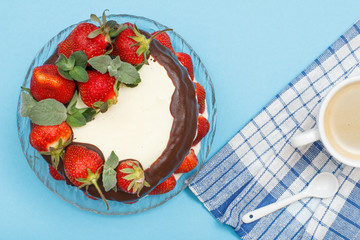 Homemade chocolate cake decorated with fresh strawberries on glass plate and cup of coffee with kitchen napkin.