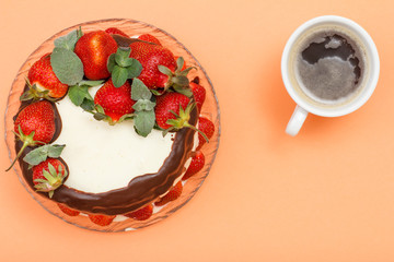 Homemade chocolate cake decorated with fresh strawberries on glass plate and cup of coffee.