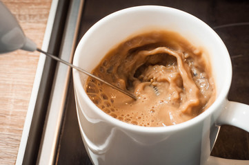 Beating cream in coffee in a white cup on the stove in the kitchen to reach the crema in the morning coffee