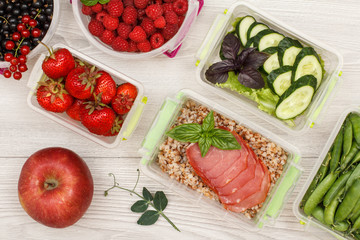 Apple and plastic meal prep containers with boiled buckwheat porridge and slices of meat, fresh vegetables and berries.