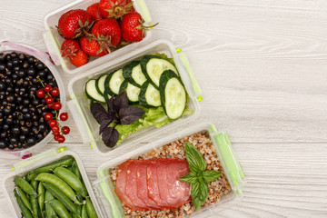 Plastic meal prep containers with boiled buckwheat porridge and slices of meat, fresh vegetables and berries.