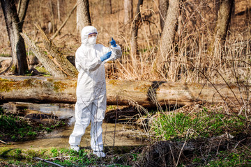 female scientist examining the liquid contents of a  test tube in the forest. Ecology and...