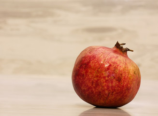 One ripe red pomegranate on a warm beige background