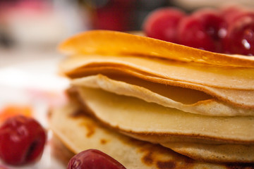 A stack of pancakes with red cherry berries close-up on a blurred background.