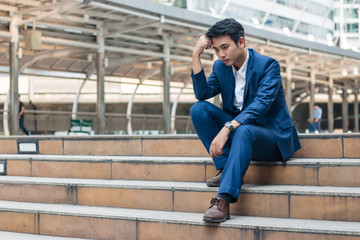 Sad yound and handsome businessman sit on the stair and have bad feeling.