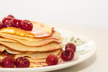 A stack of thin pancakes with red cherry berries on a plate on a white background