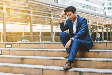 Sad yound and handsome businessman sit on the stair and have bad feeling.