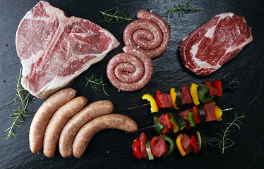 Assorted delicious raw meat with vegetable on a barbecue with t-bone steak, sausages and meat...