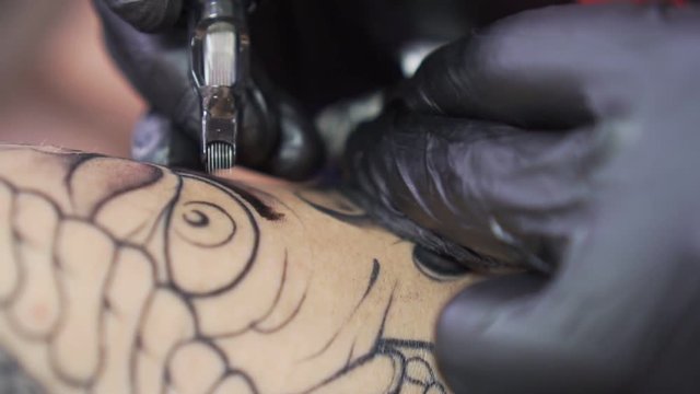 process of tattooing close-up. The needle of the tattoo machine inserts ink under the skin.