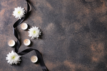 Black mourning ribbon, flowers and candles on grunge background