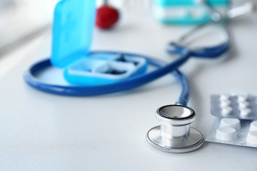 Stethoscope and pills on table in clinic, closeup