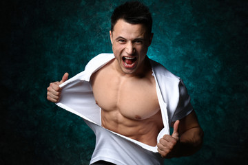 Sporty man tearing his t-shirt on dark background