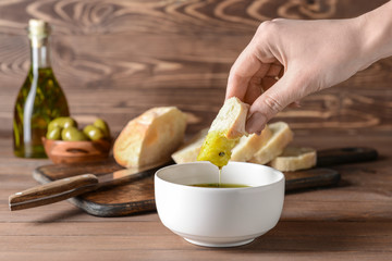 Woman dipping fresh bread into tasty olive oil in bowl